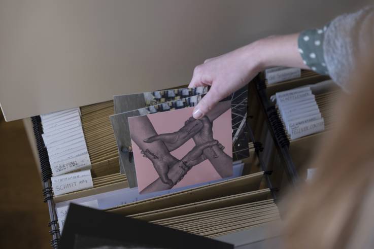Une main tient des reproductions d'oeuvres d'art rangées dans un meuble de classement